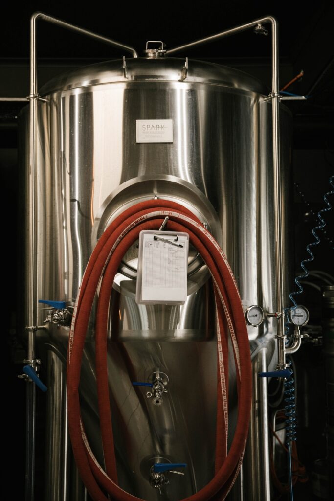 Fermentation tank in a brewery with hoses and a brew log hanging off the manway door