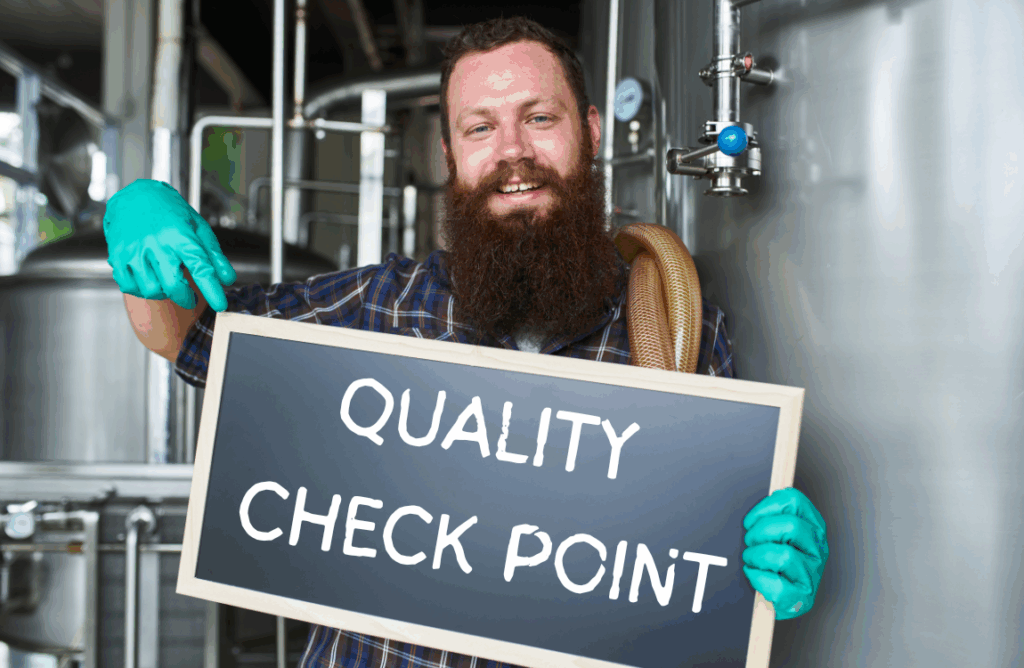 Brewer in a brewery holding a sign that reads, "Quality Check Point"