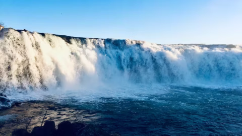 A photo of a wide waterfall with a blue sky behind it.